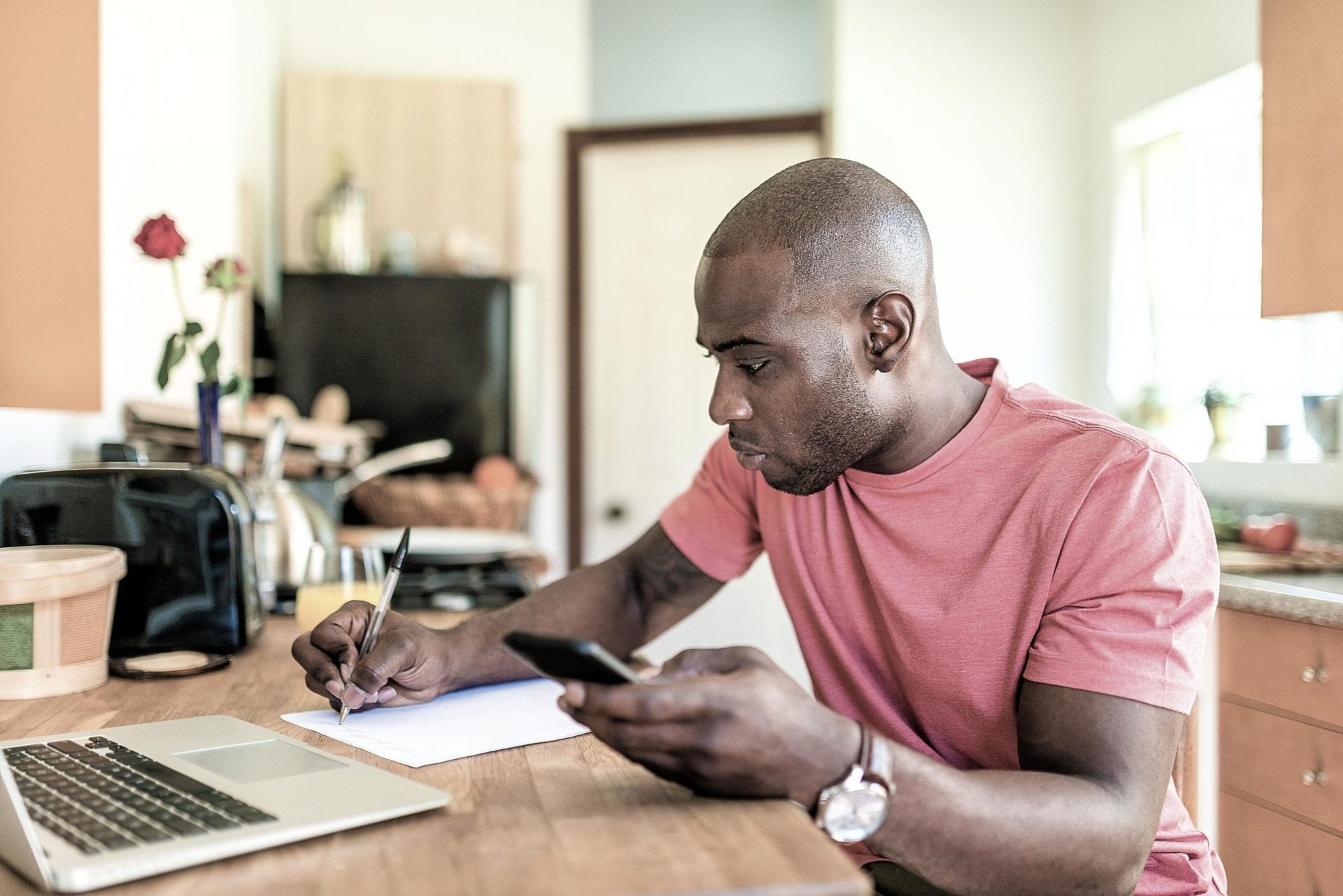 car shopper writing down pricing details while looking at computer and phone